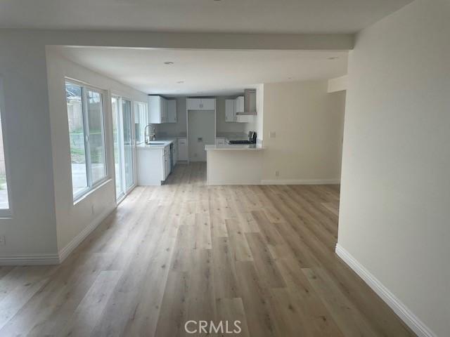 unfurnished living room with a sink, baseboards, and light wood-style flooring