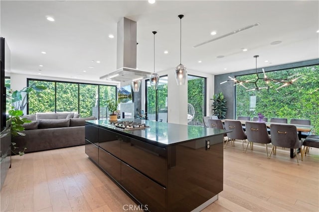 kitchen with island exhaust hood, light wood-type flooring, stainless steel gas cooktop, hanging light fixtures, and a large island