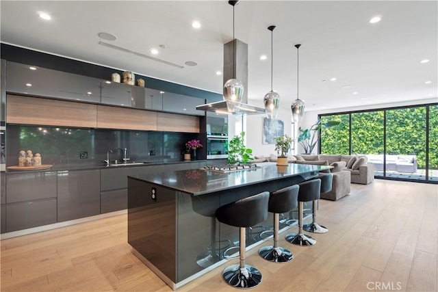 kitchen featuring decorative backsplash, light wood-type flooring, island range hood, a spacious island, and pendant lighting