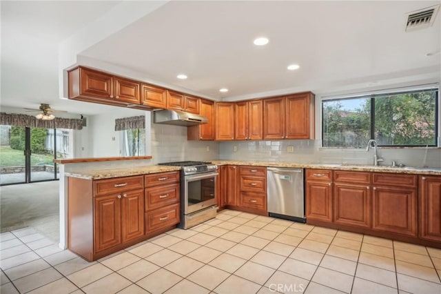 kitchen featuring sink, stainless steel appliances, light stone countertops, decorative backsplash, and kitchen peninsula