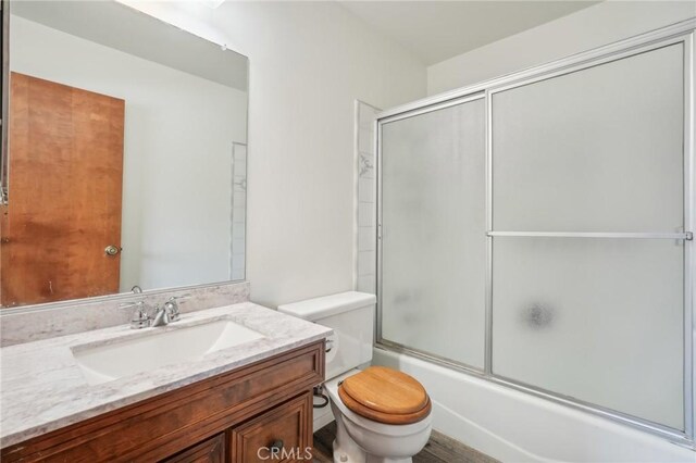 full bathroom with hardwood / wood-style floors, vanity, toilet, and enclosed tub / shower combo