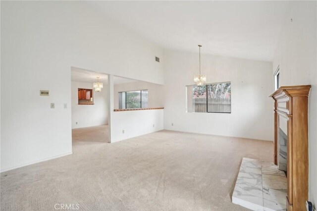 unfurnished living room with high vaulted ceiling, light colored carpet, and a notable chandelier