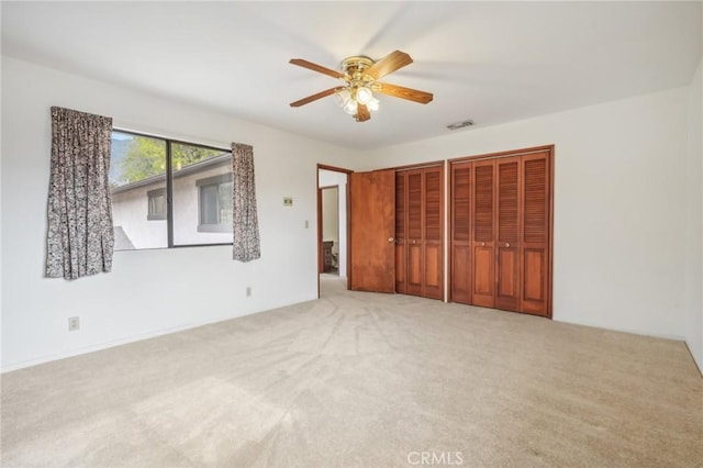 unfurnished bedroom with ceiling fan, light carpet, and multiple closets