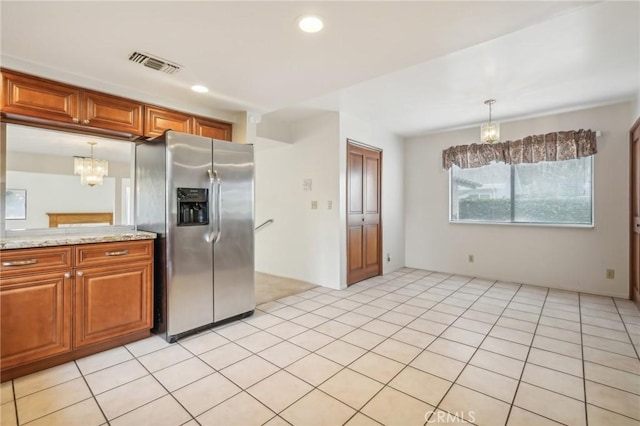 kitchen with an inviting chandelier, hanging light fixtures, stainless steel fridge, light stone countertops, and light tile patterned floors