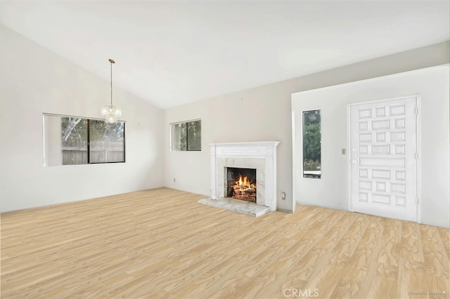 unfurnished living room with lofted ceiling, a fireplace, light hardwood / wood-style floors, and a chandelier