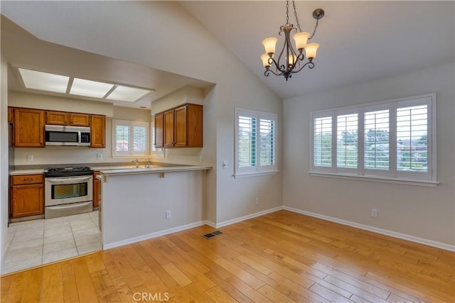 kitchen featuring vaulted ceiling, appliances with stainless steel finishes, hanging light fixtures, kitchen peninsula, and light hardwood / wood-style flooring