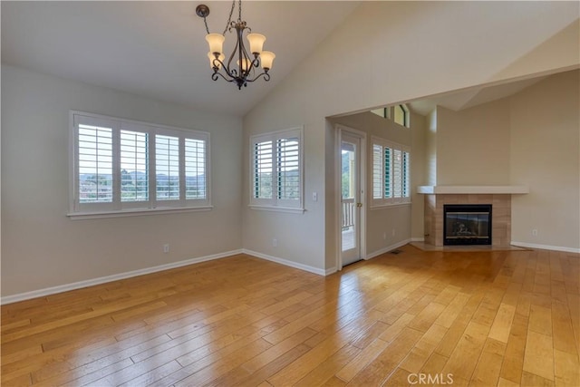 unfurnished living room featuring a chandelier, a tiled fireplace, high vaulted ceiling, and light hardwood / wood-style flooring