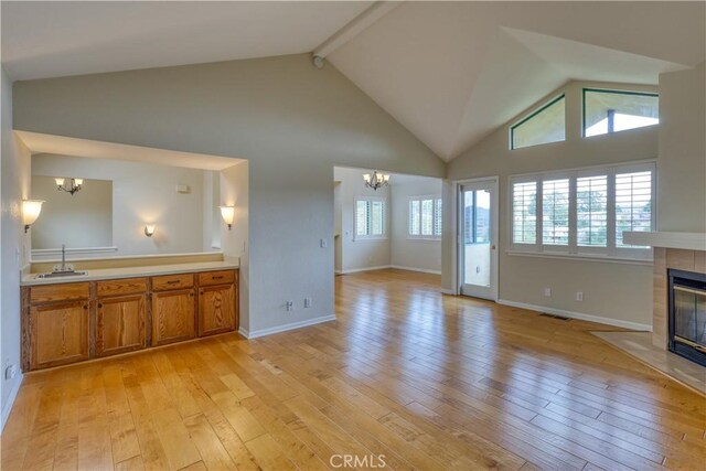 unfurnished living room with a tiled fireplace, a healthy amount of sunlight, a chandelier, and light hardwood / wood-style floors