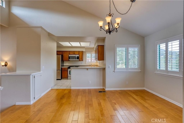 kitchen with lofted ceiling, hanging light fixtures, kitchen peninsula, stainless steel appliances, and light hardwood / wood-style floors