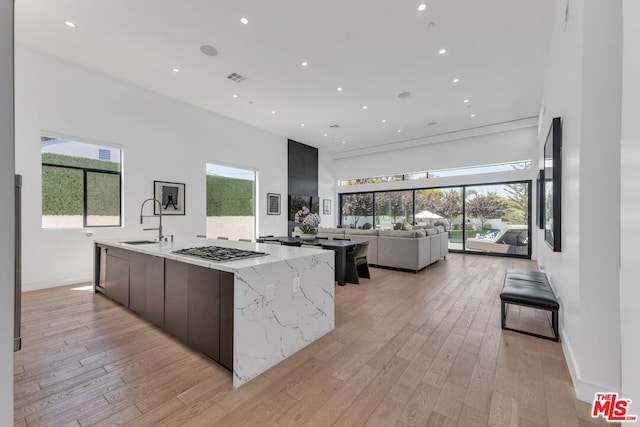 kitchen featuring stainless steel gas stovetop, sink, a large island, light hardwood / wood-style floors, and light stone counters