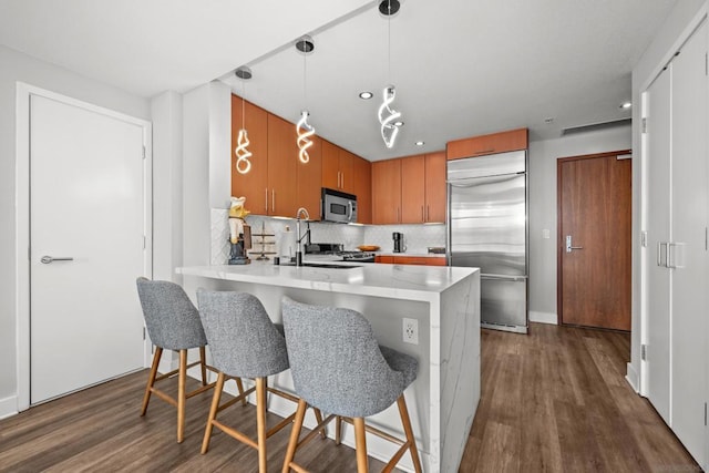 kitchen featuring pendant lighting, dark hardwood / wood-style floors, decorative backsplash, kitchen peninsula, and stainless steel appliances