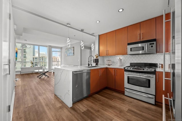 kitchen with kitchen peninsula, stainless steel appliances, hardwood / wood-style flooring, and sink