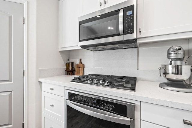 kitchen with white cabinets, backsplash, light stone countertops, and stainless steel appliances