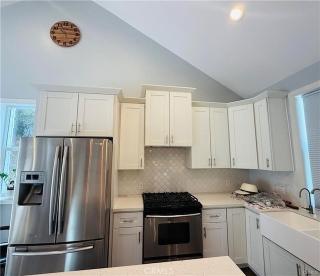 kitchen with lofted ceiling, backsplash, white cabinets, sink, and stainless steel appliances