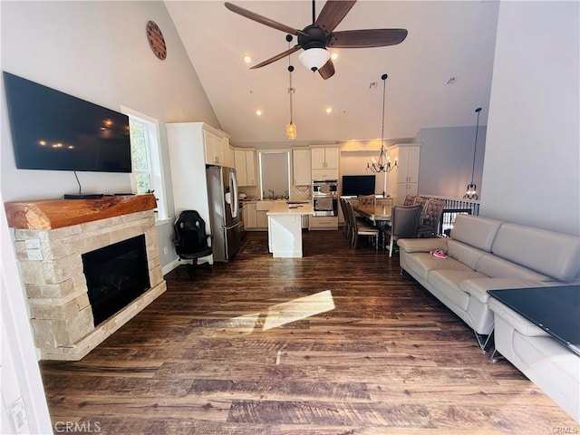 living room featuring ceiling fan with notable chandelier, a stone fireplace, dark wood-type flooring, and high vaulted ceiling