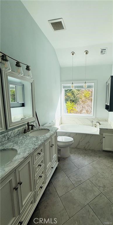 bathroom featuring vanity, vaulted ceiling, tiled tub, tile patterned flooring, and toilet