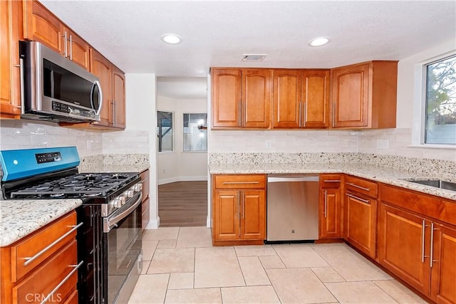 kitchen with light stone countertops, appliances with stainless steel finishes, and tasteful backsplash