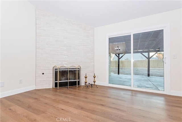 unfurnished living room featuring wood-type flooring, a brick fireplace, and brick wall