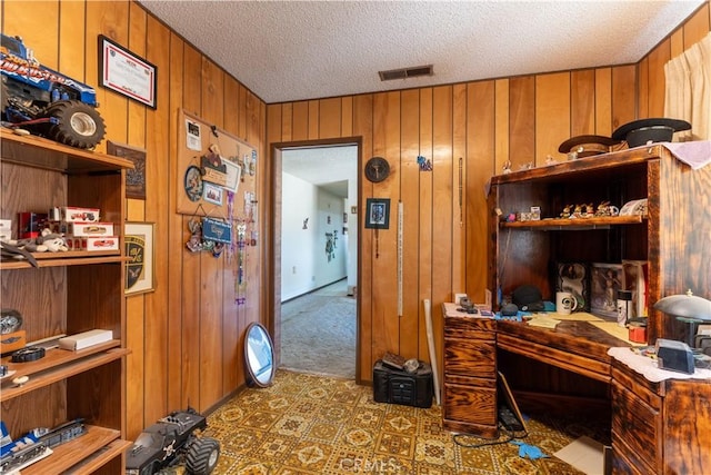 carpeted office space with wooden walls and a textured ceiling