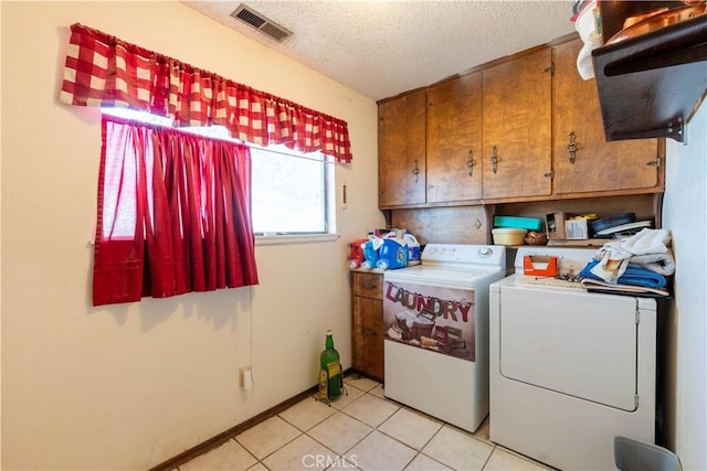 laundry room featuring washing machine and dryer, light tile patterned flooring, a textured ceiling, and cabinets