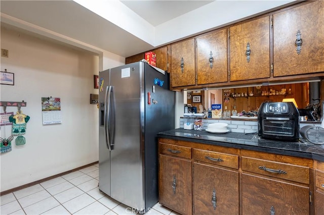 kitchen with light tile patterned flooring, dark stone countertops, and stainless steel fridge