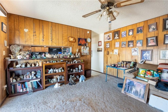 interior space featuring a textured ceiling, ceiling fan, wooden walls, and light carpet