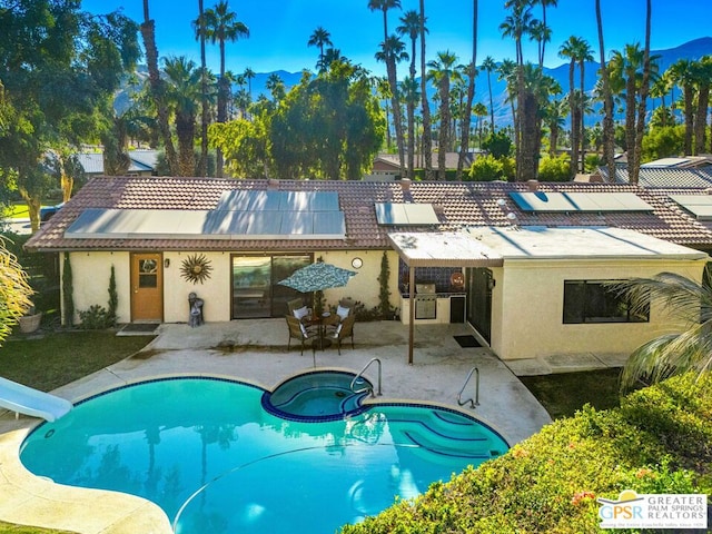 rear view of property featuring solar panels, a patio, and a swimming pool with hot tub