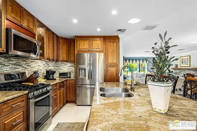 kitchen featuring light stone countertops, backsplash, stainless steel appliances, sink, and light tile patterned flooring