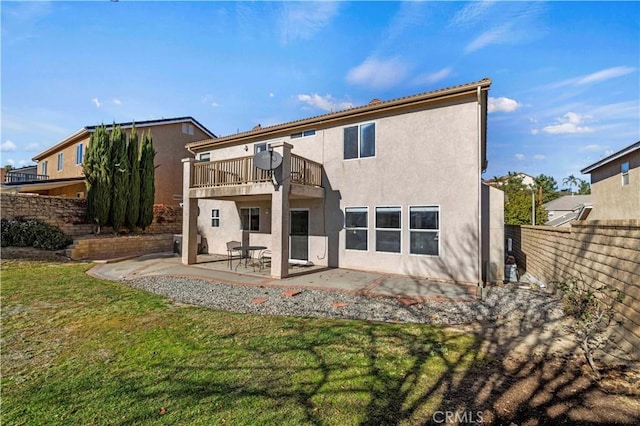 rear view of house featuring a lawn, a balcony, and a patio