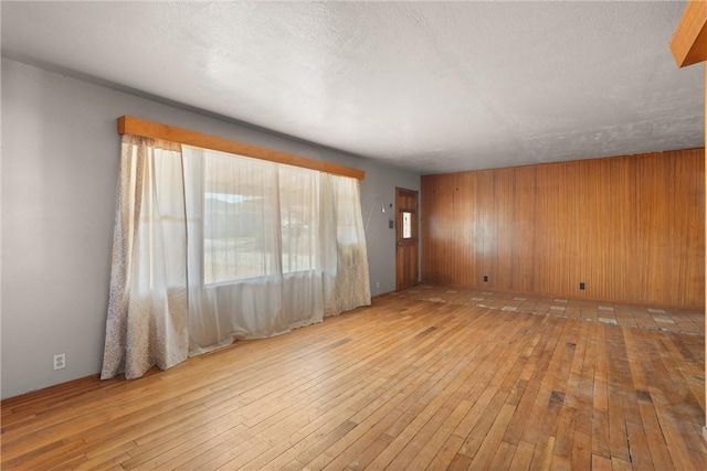 unfurnished room featuring wood walls, light hardwood / wood-style floors, and a textured ceiling