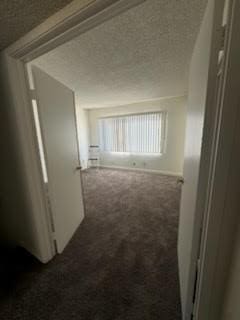 corridor featuring dark colored carpet and a textured ceiling