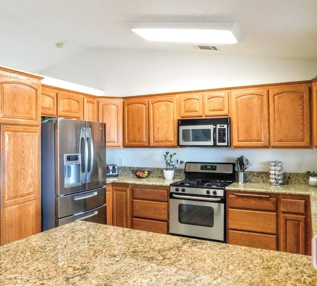 kitchen featuring vaulted ceiling, appliances with stainless steel finishes, and light stone counters