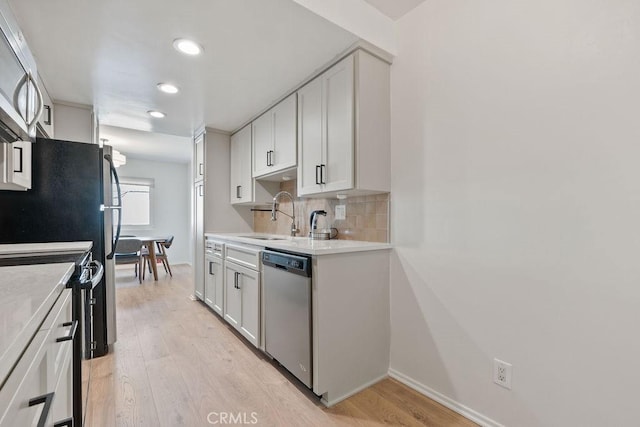 kitchen featuring tasteful backsplash, white cabinets, stainless steel appliances, light countertops, and a sink