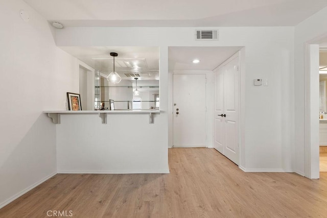 kitchen featuring baseboards, light wood-style flooring, a kitchen breakfast bar, decorative light fixtures, and a peninsula