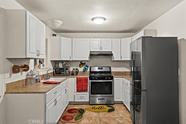 kitchen with appliances with stainless steel finishes, a textured ceiling, sink, light tile patterned floors, and white cabinetry