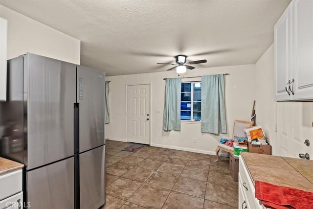 kitchen with a textured ceiling, ceiling fan, tile countertops, white cabinetry, and stainless steel refrigerator