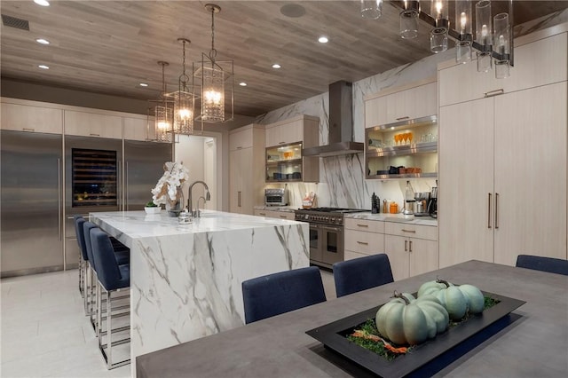 kitchen featuring high end appliances, modern cabinets, a breakfast bar area, and wall chimney exhaust hood