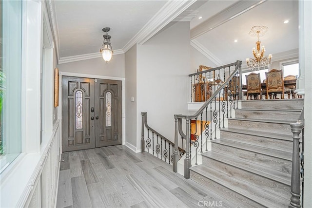 foyer entrance featuring a chandelier, lofted ceiling, crown molding, and light wood-style flooring