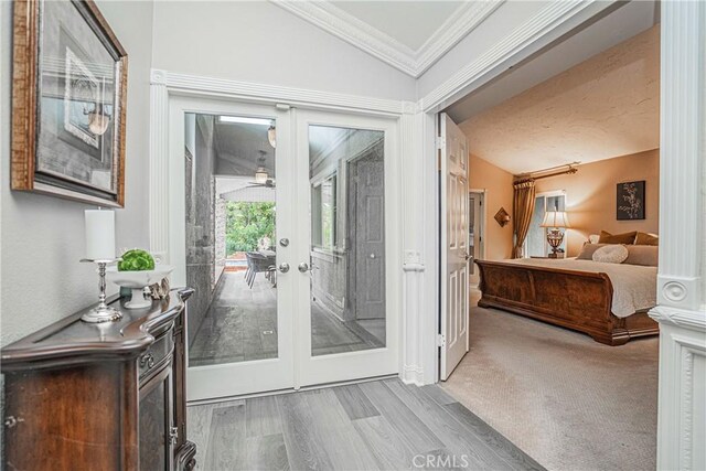 entryway featuring vaulted ceiling, ornamental molding, french doors, and light wood-type flooring