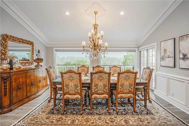 dining space with light wood finished floors, a notable chandelier, crown molding, and wainscoting