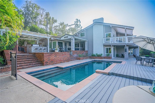 rear view of house with exterior bar, an outdoor kitchen, a patio area, a balcony, and a pergola