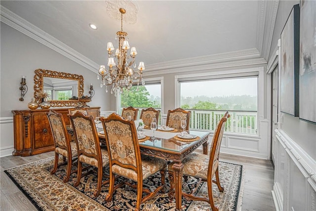 dining area with lofted ceiling, a decorative wall, a notable chandelier, wood finished floors, and ornamental molding