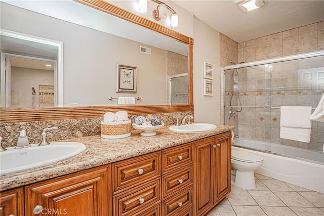 bathroom with double vanity, bath / shower combo with glass door, a sink, and tile patterned floors