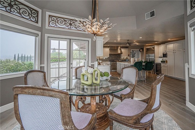 dining area with light wood finished floors, baseboards, visible vents, french doors, and a notable chandelier