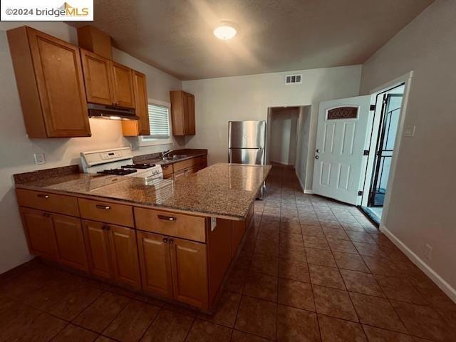 kitchen with white range oven, sink, stone countertops, dark tile patterned flooring, and stainless steel refrigerator