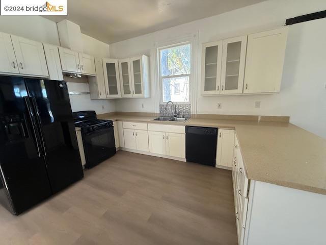 kitchen featuring black appliances, white cabinetry, sink, and light hardwood / wood-style flooring