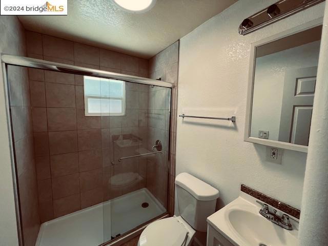 bathroom with a textured ceiling, vanity, toilet, and a shower with door