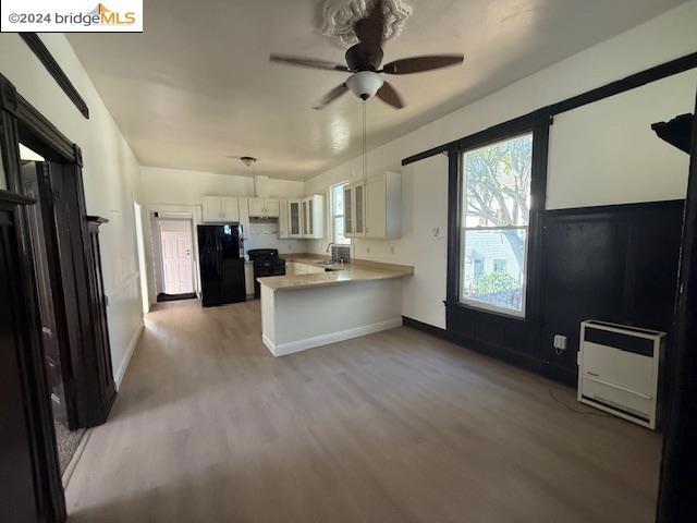 kitchen with kitchen peninsula, heating unit, white cabinets, black appliances, and hardwood / wood-style flooring