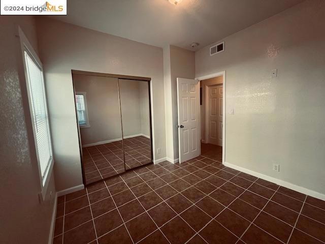 unfurnished bedroom featuring multiple windows, a closet, and dark tile patterned flooring