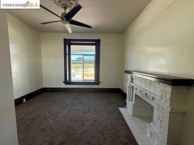 unfurnished living room with dark colored carpet, ceiling fan, and a tiled fireplace